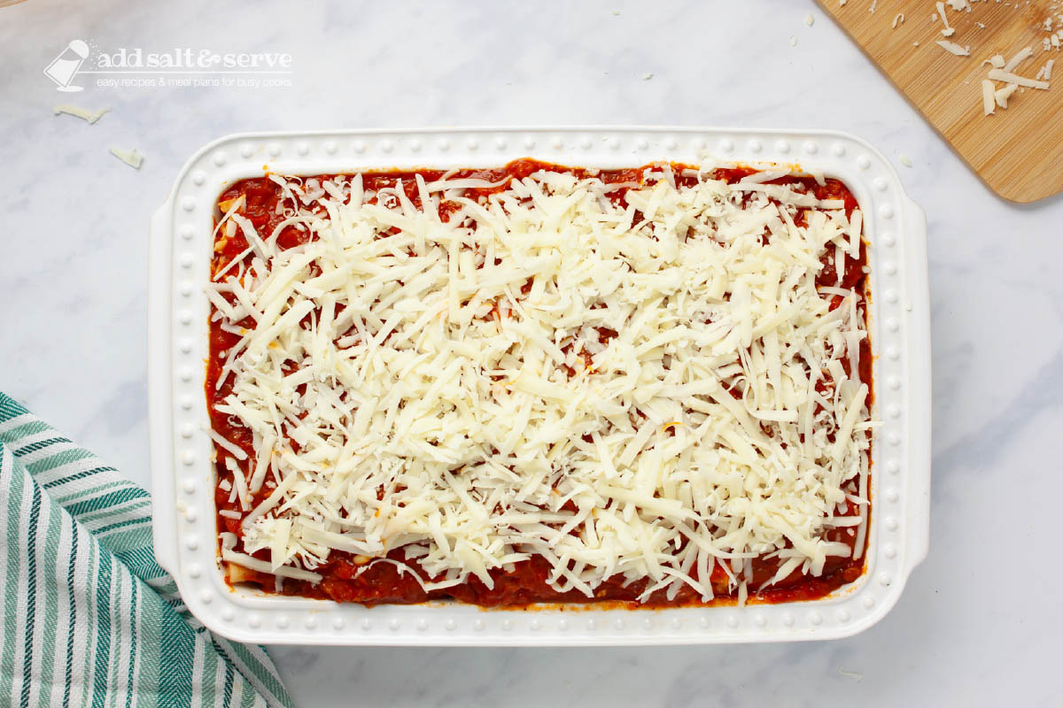 Baking pan showing mozzarella cheese layered over marinara sauce for baked ziti.