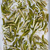 roasted okra and onions on parchment paper on a sheet pan.