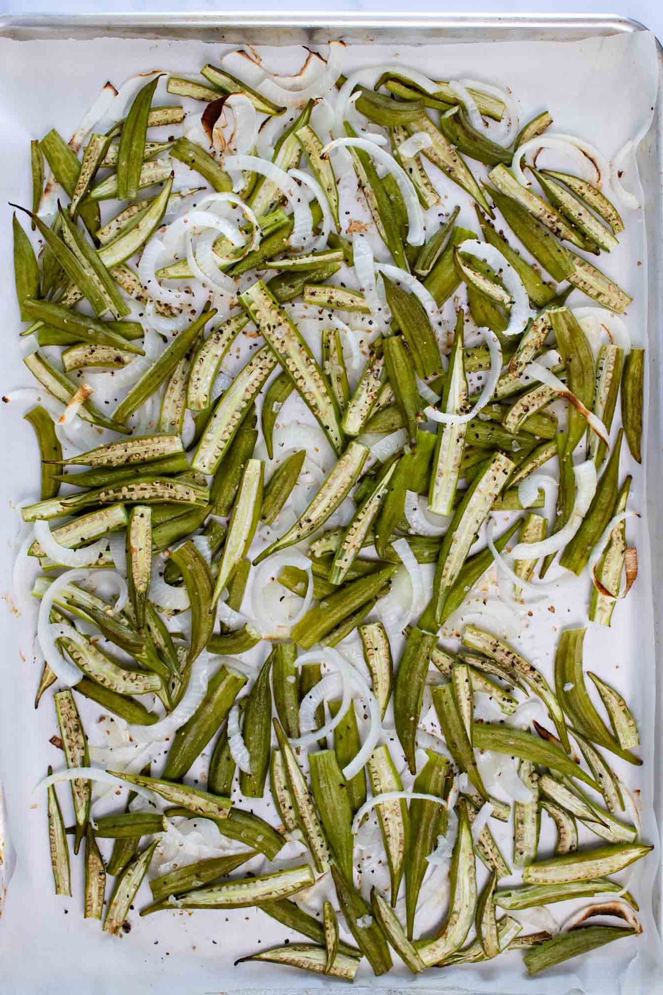 roasted sliced okra and onions on parchment paper on a sheet pan.