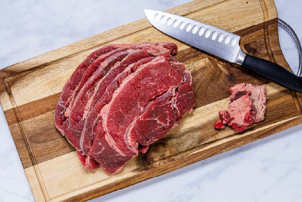 Slices of chuck roast on a cutting board with excess fat cut off.