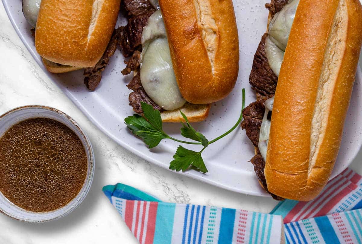 A plate of French Dip sandwiches beside a bowl of au jus.